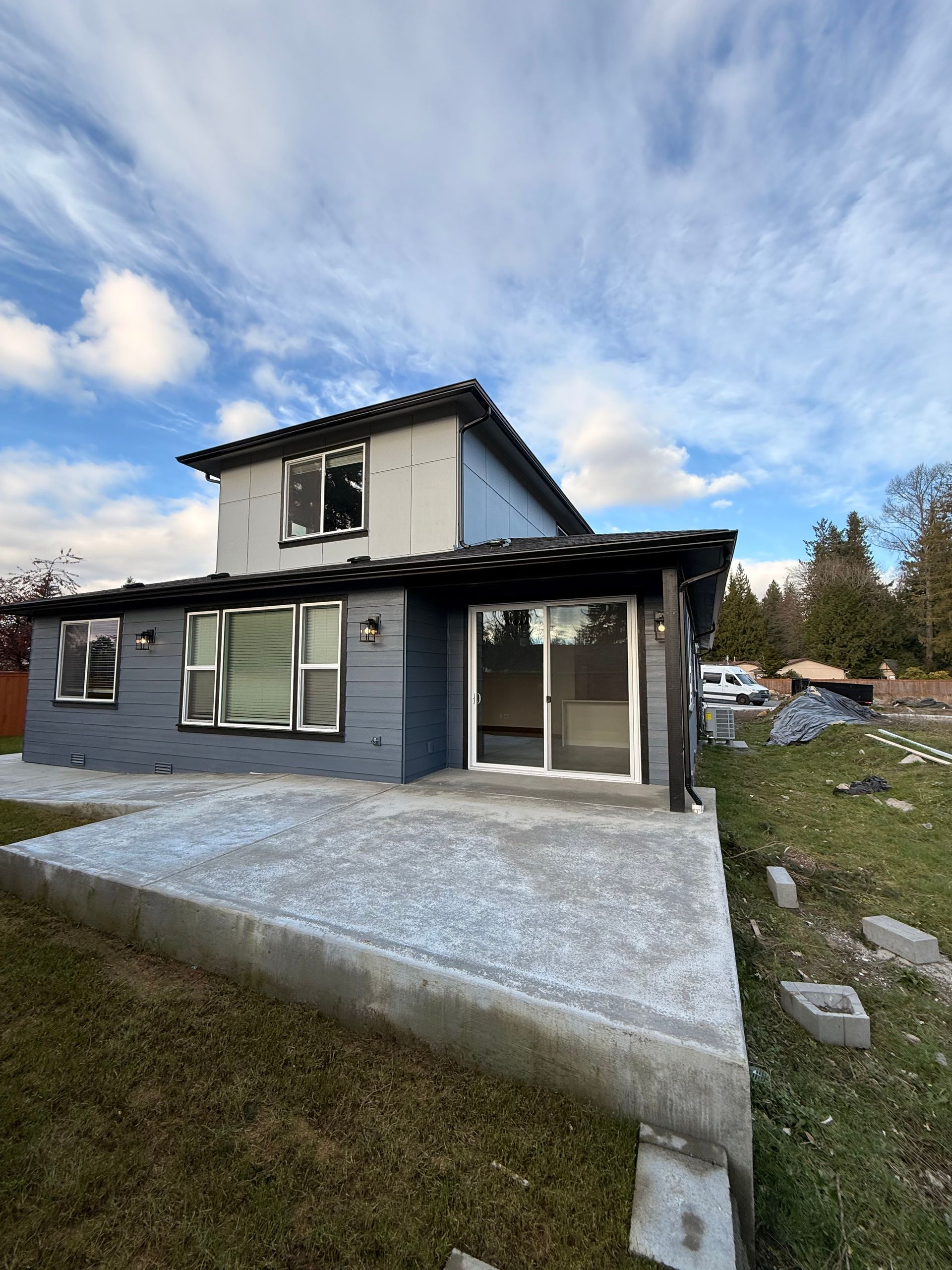 Construction worker in trench, installing drainage pipe. Dirt, plastic sheeting, and machinery visible. Cloudy day.