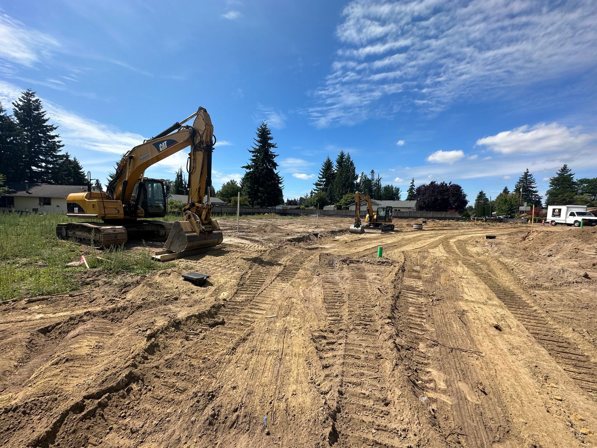 Construction site with two excavators on a cleared lot under a blue sky.