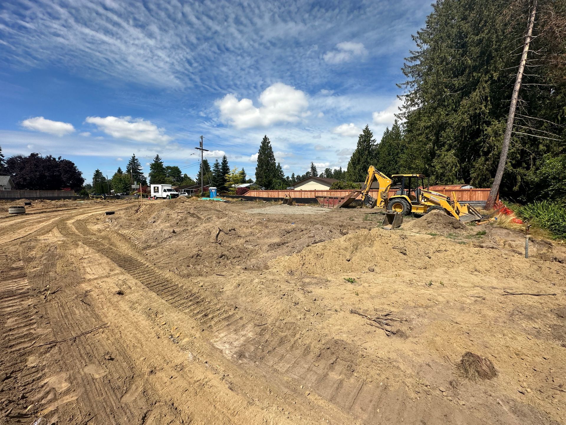 Construction site with dirt piles, excavator, and blue sky.