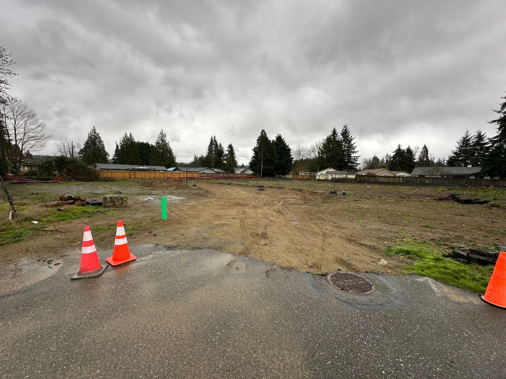 Cleared lot with orange cones on pavement, overcast sky, trees in the background.
