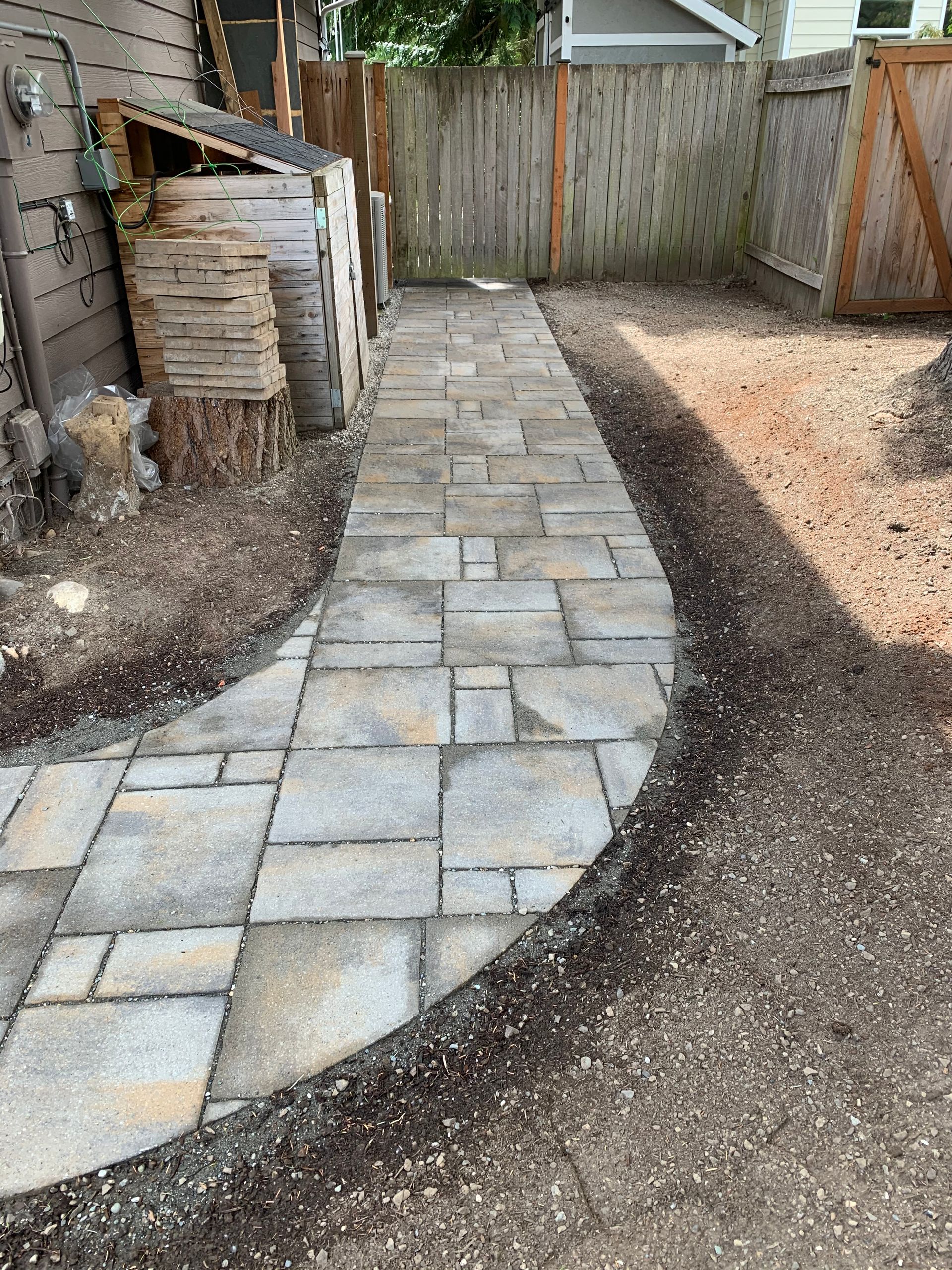 Stone path leading through a yard, bordered by dirt and fence.