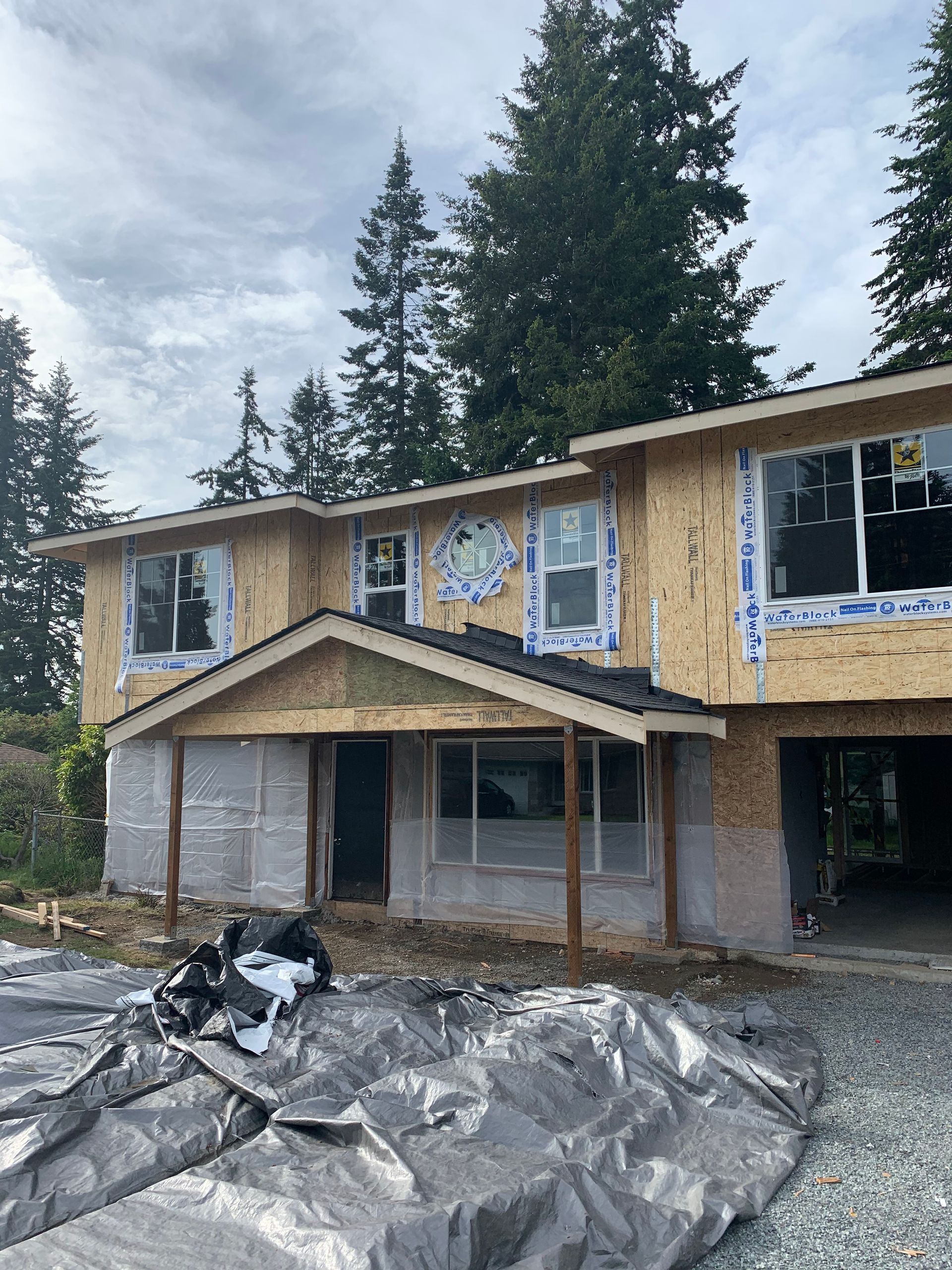 Two-story house under construction; exposed wood frame, windows installed, and a porch. 