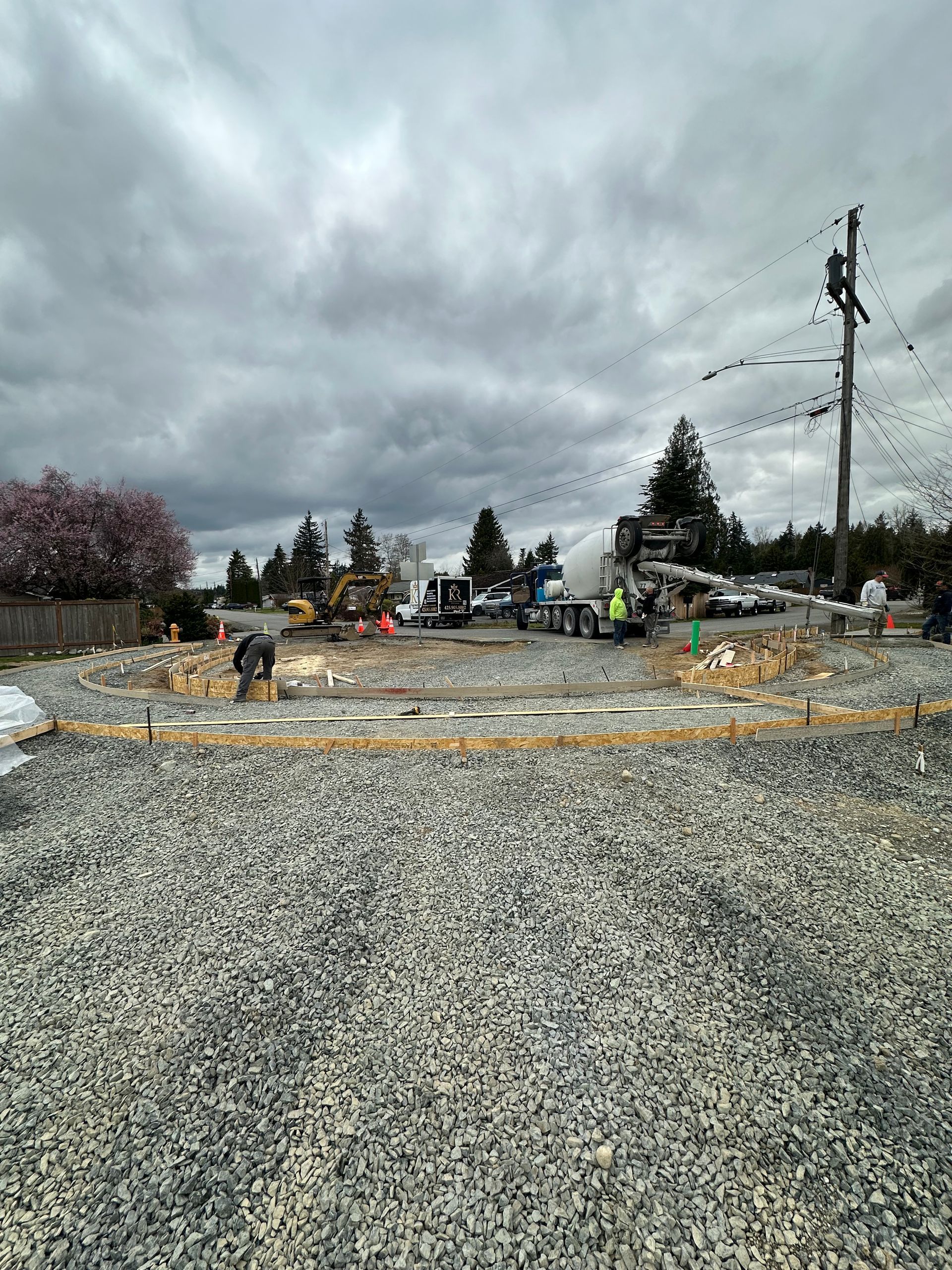 Construction site with gravel foreground, heavy machinery, cloudy sky.