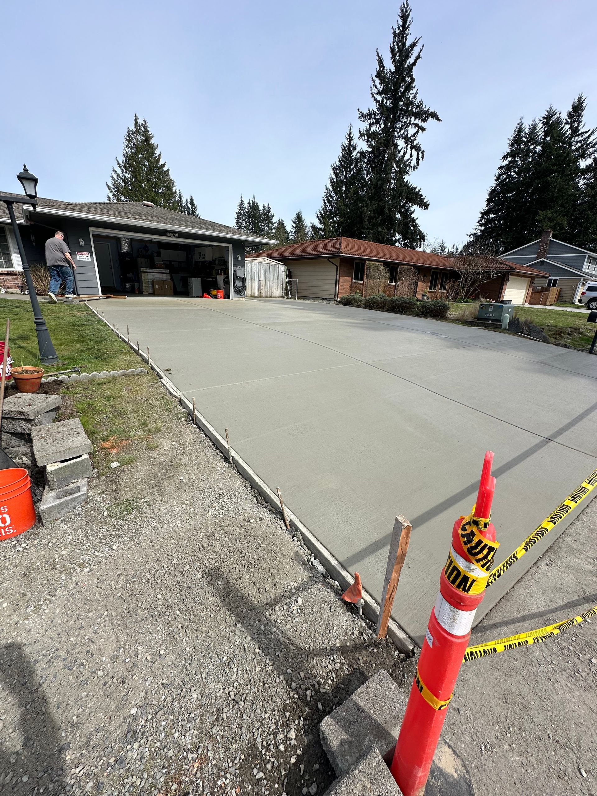 Freshly poured concrete driveway in front of a house. Red cone and caution tape on the right.