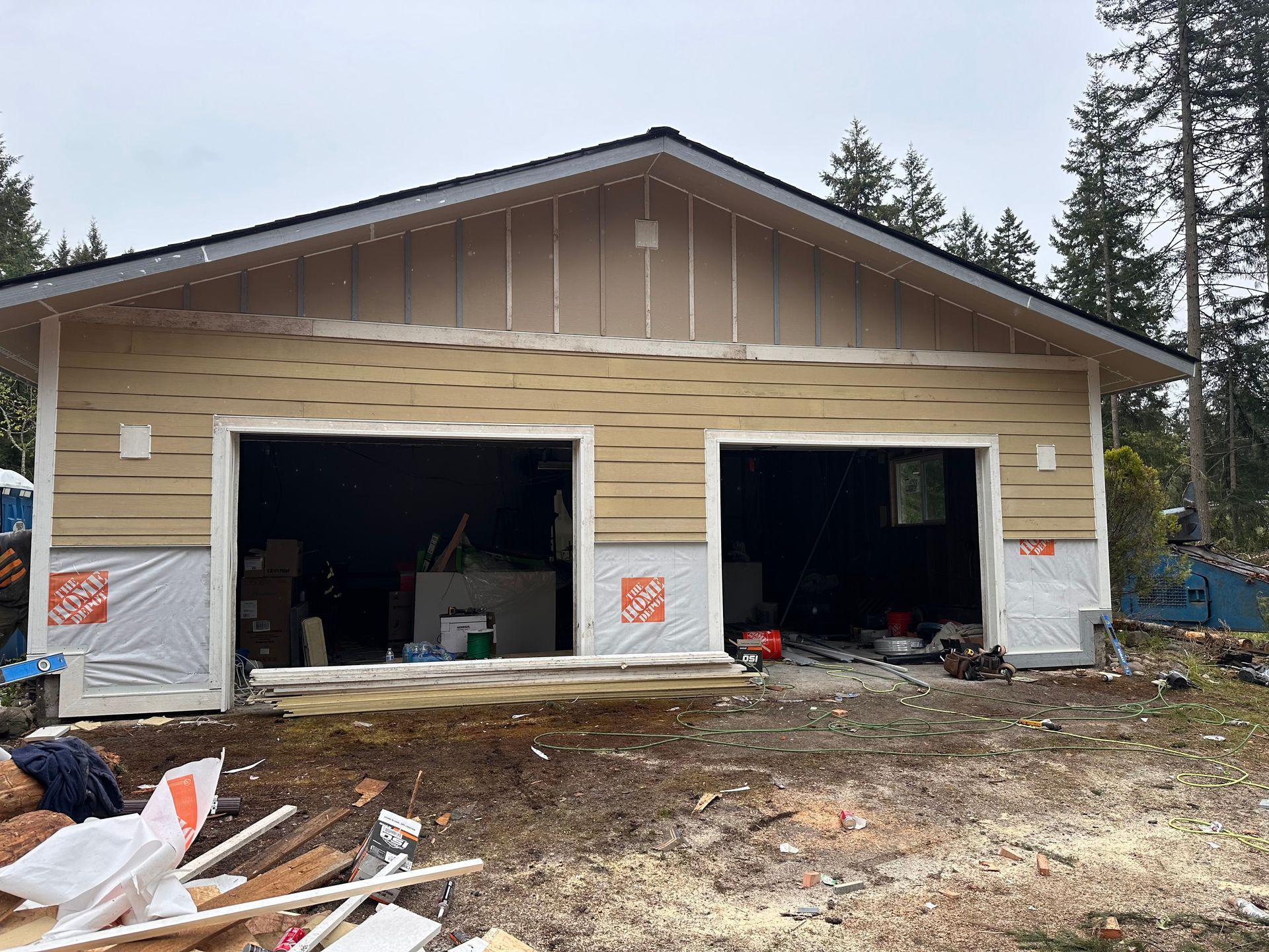 Two-car garage under construction with tan siding, open garage doors, and unfinished interior.