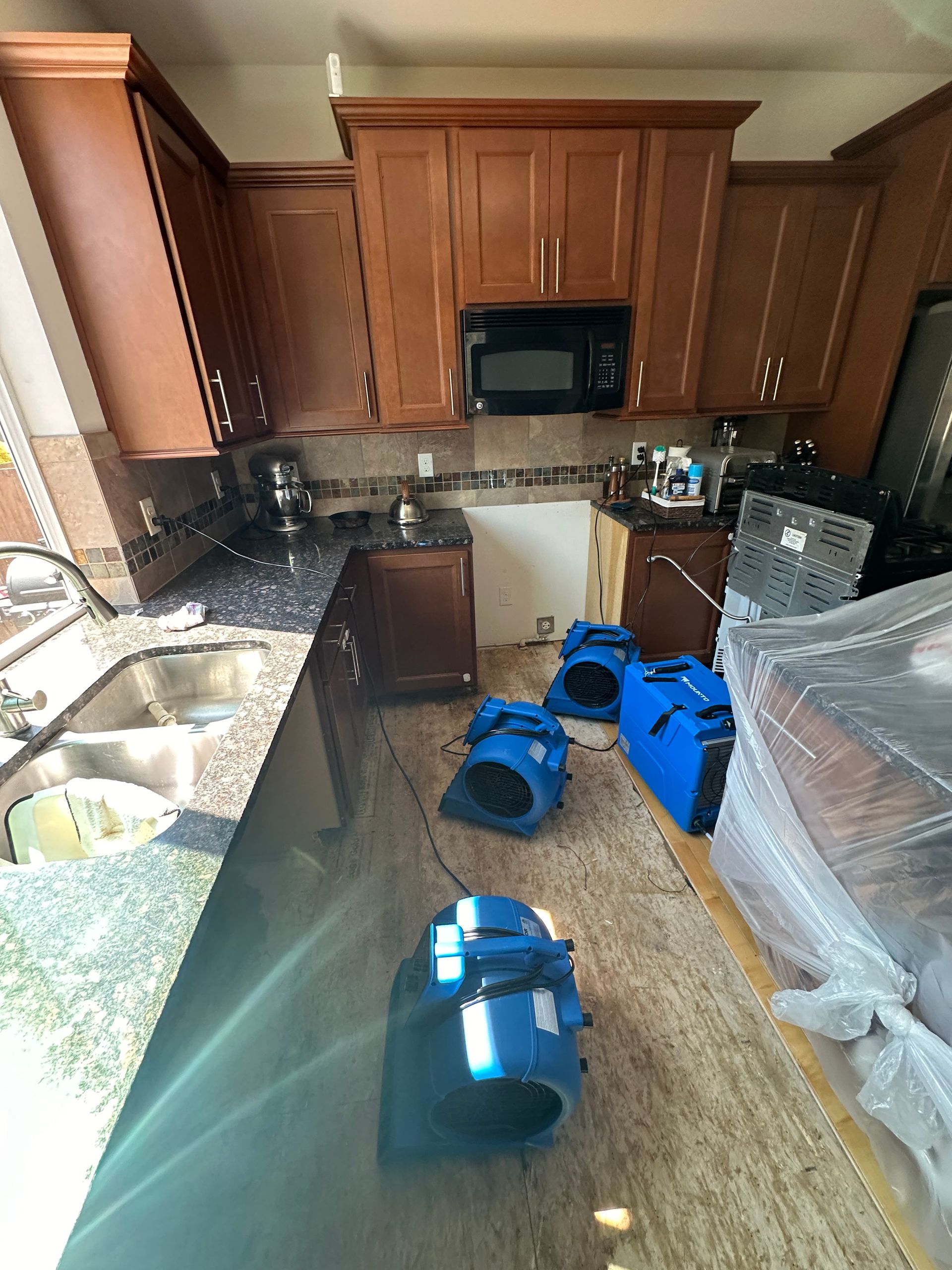 Kitchen with cabinets, countertops, and drying equipment on the floor; microwave above an open space.