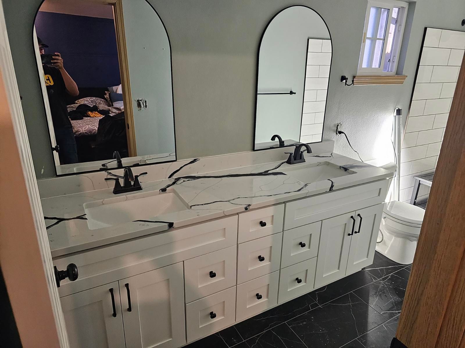 Bathroom with white double vanity, black fixtures, arched mirrors, and marble countertop.