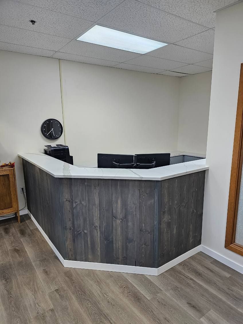 Reception desk with gray wood paneling and white countertop in an office setting.