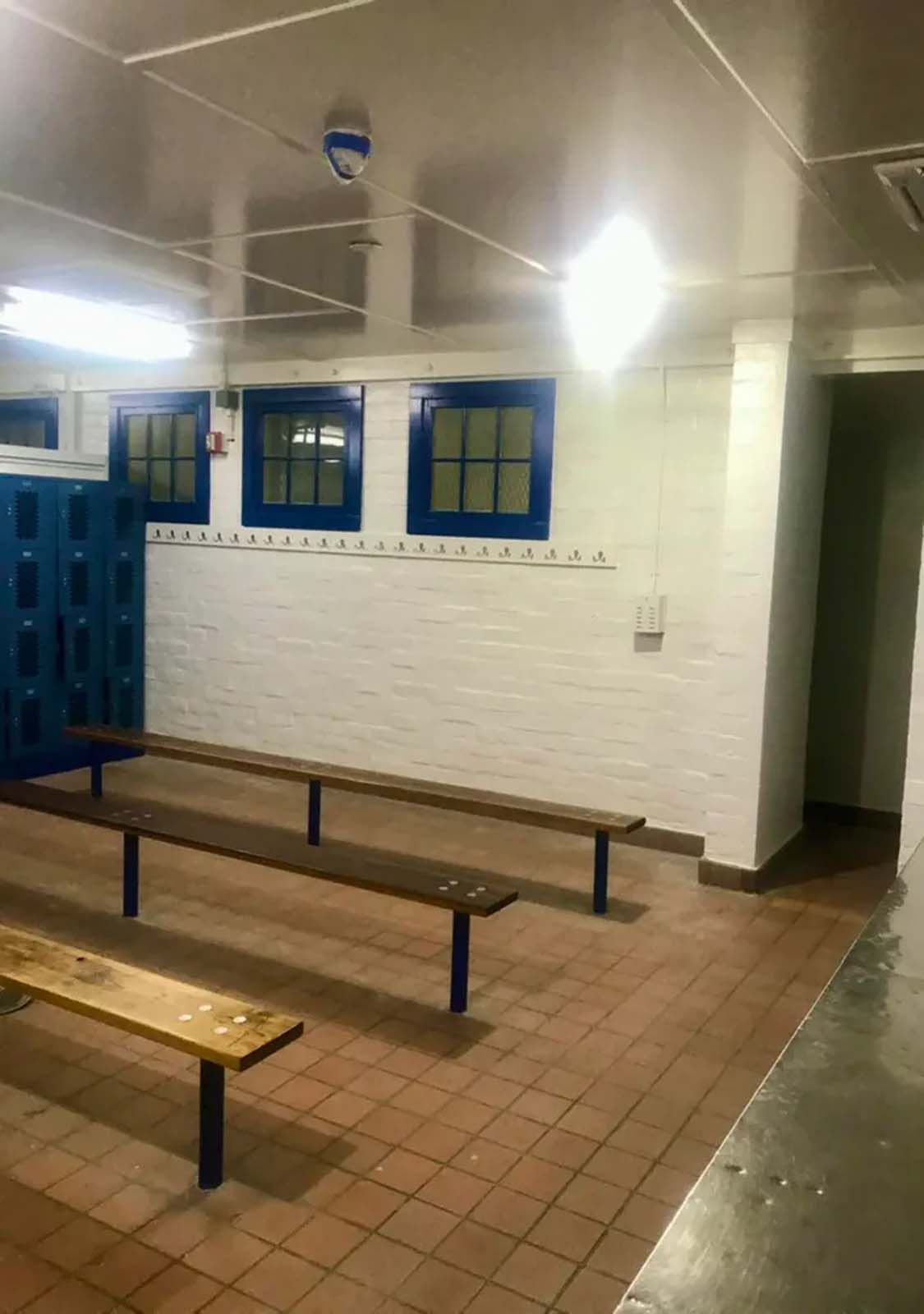 A locker room with wooden benches and blue lockers.