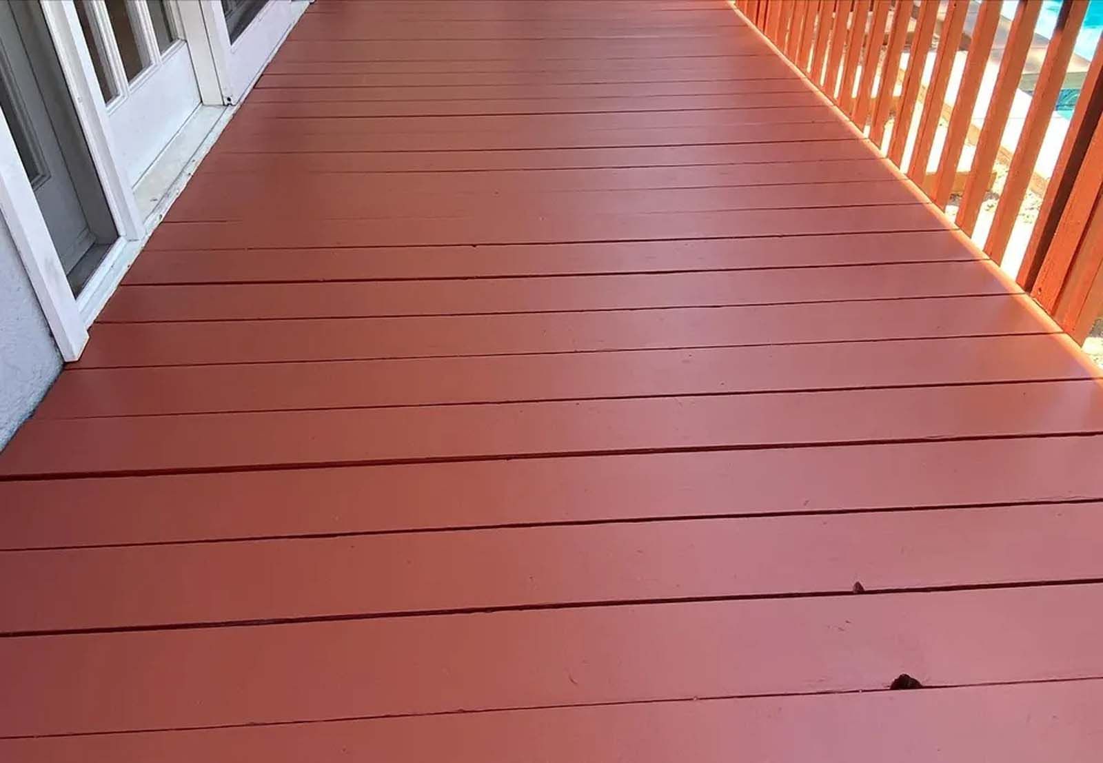 A red wooden deck with a white railing and a pool in the background.