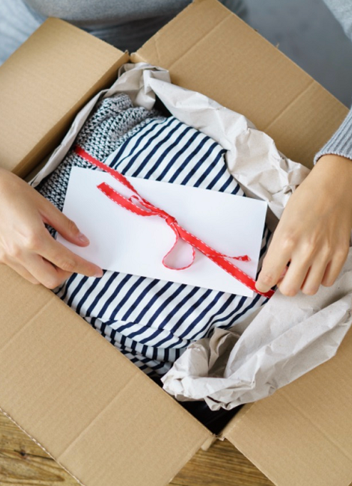 A person is putting a striped shirt in a cardboard box.