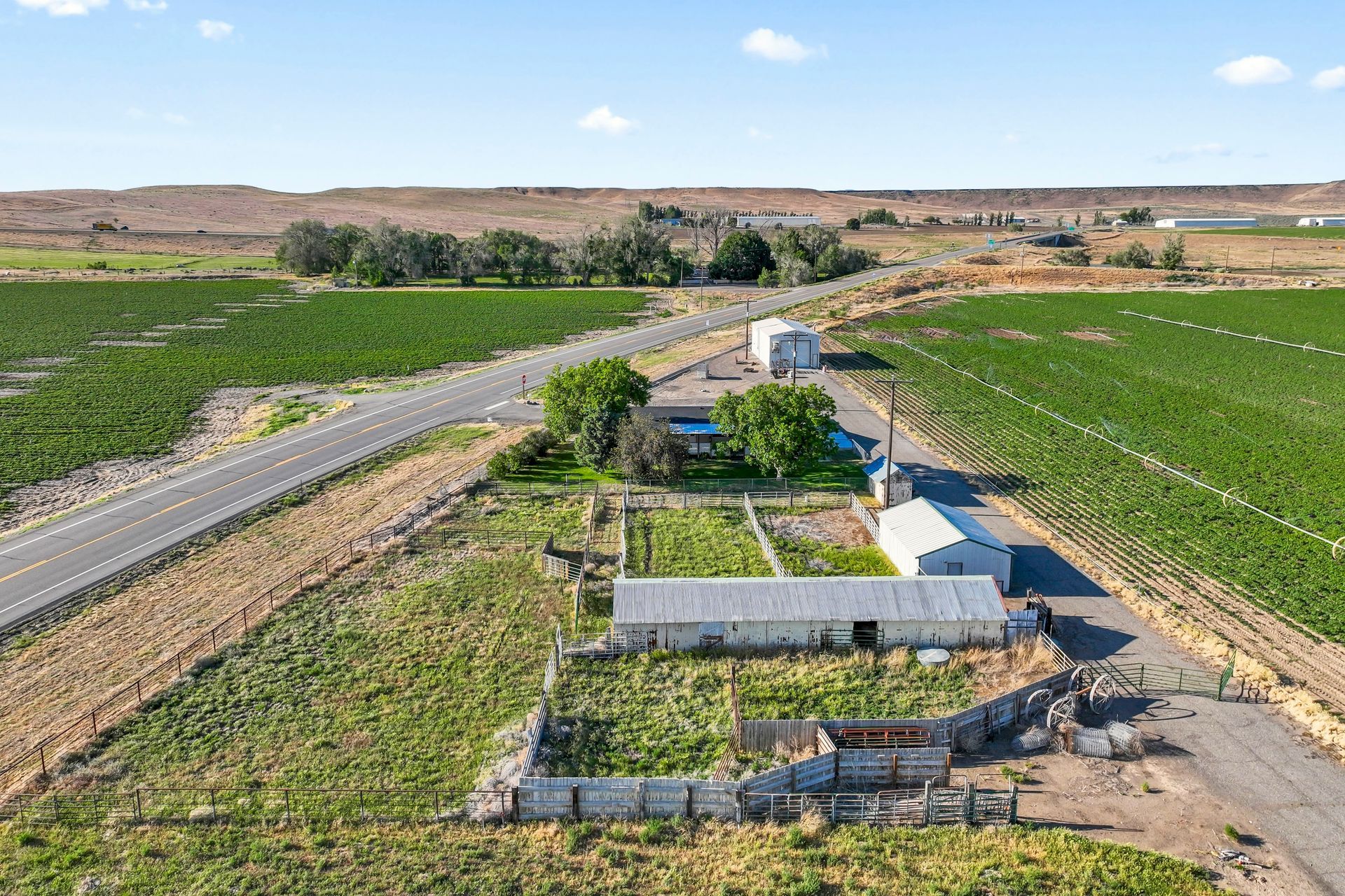 Aerial view of a farm with a house, pool, and fields, alongside a road in a rural landscape.
