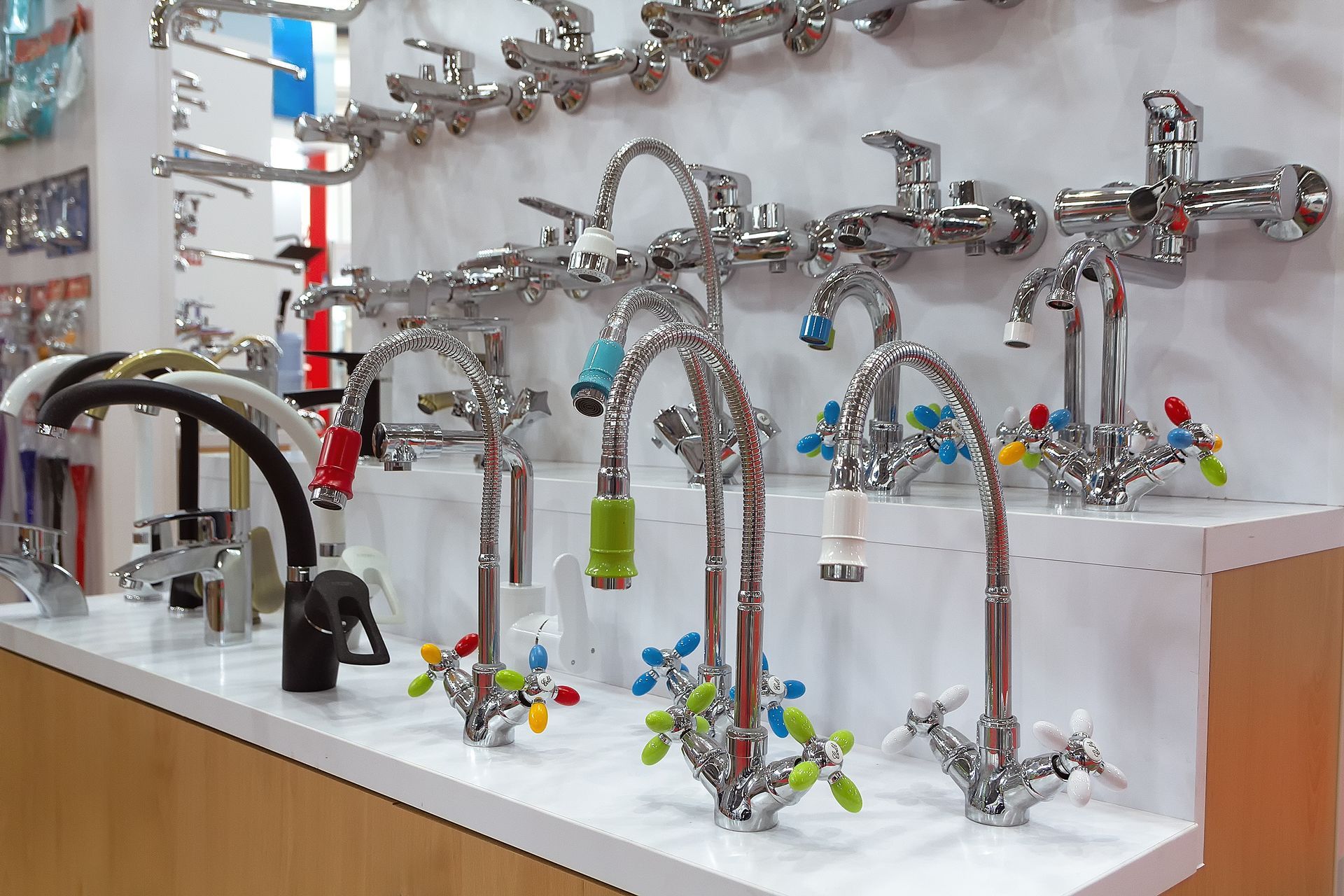 Display of various chrome faucets in a store setting, featuring several designs with colorful handles.