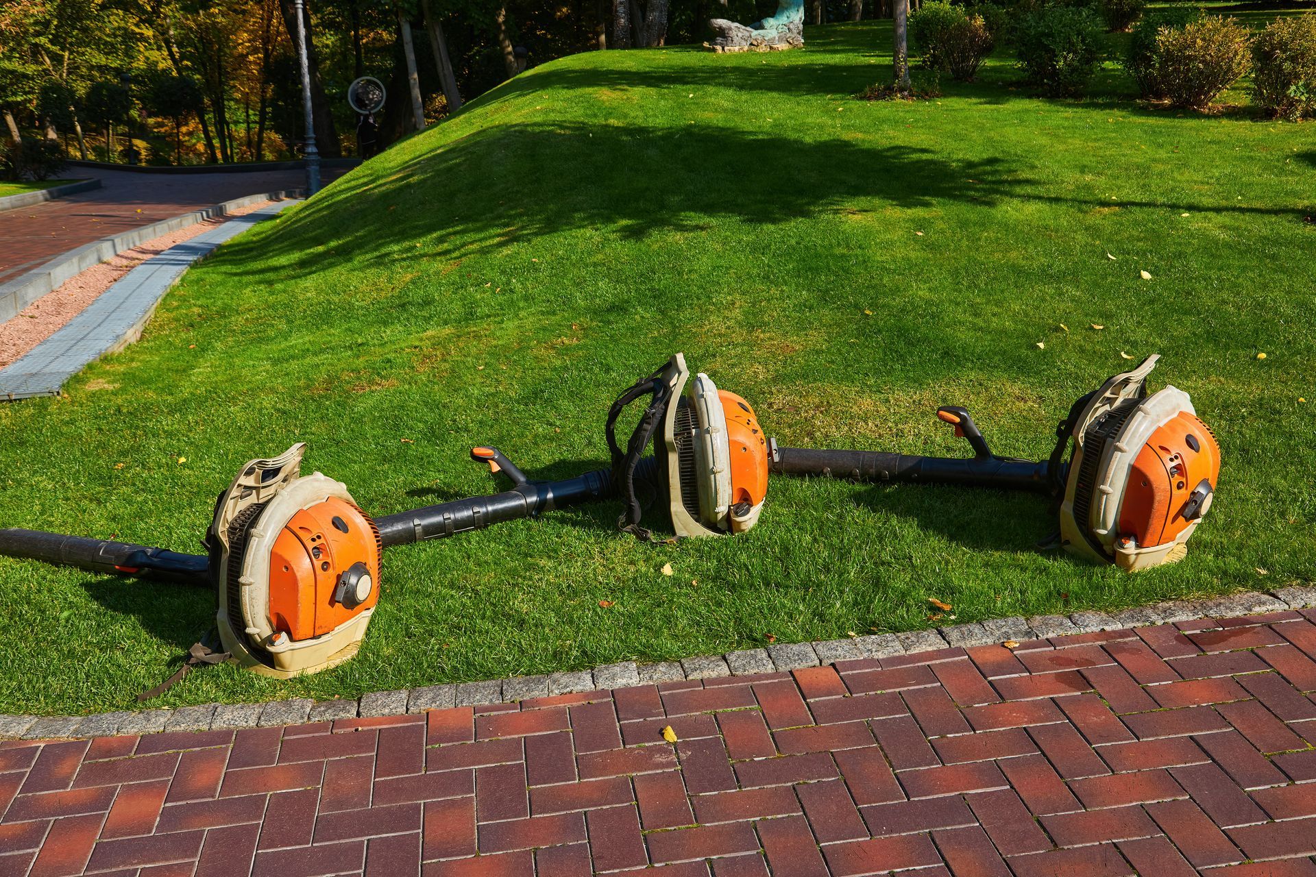Three orange and brown pump-shaped objects connected by black pipes on a grassy hill with brick pavement.