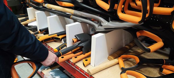 Person reaching for a shovel with an orange handle in a store display.