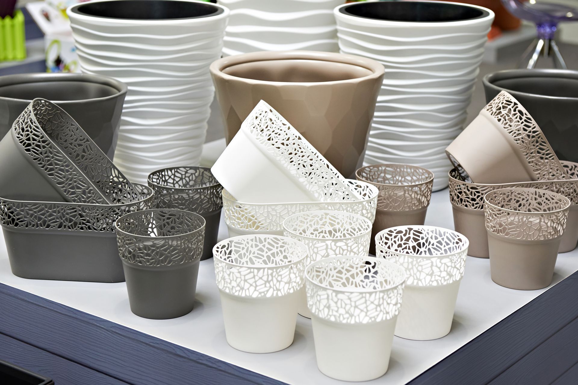 Flower pots in various sizes and colors, including white, gray, and beige. Some feature decorative patterns.