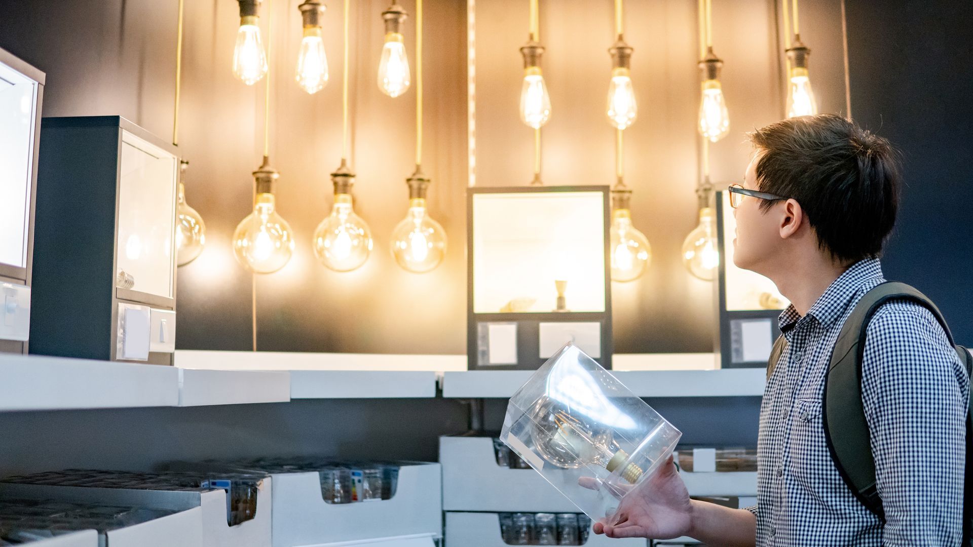 Man in glasses looks at display case with lights and a model inside.