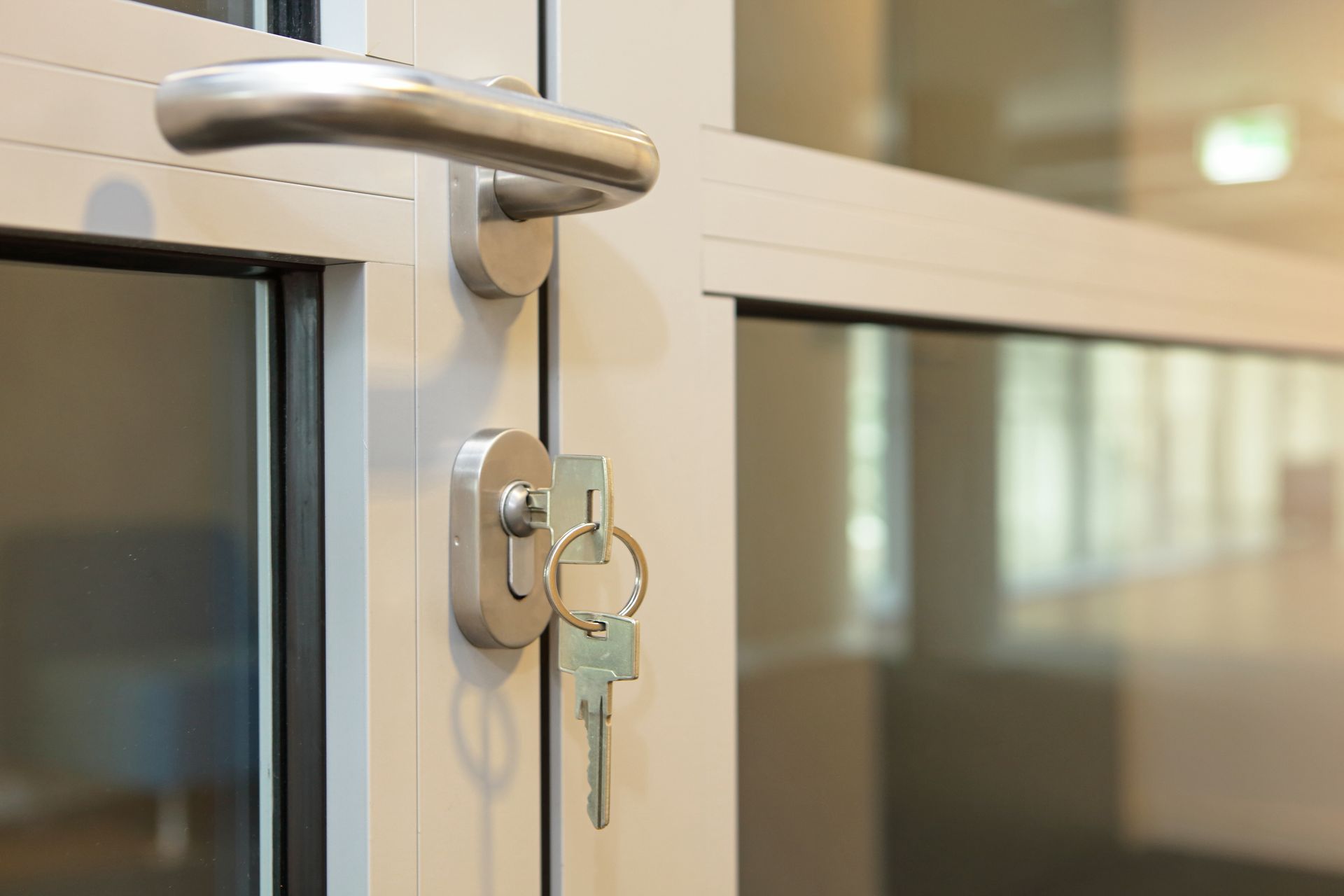 Close-up of a door handle, key in the lock, and glass panels. The door frame is white and metal.