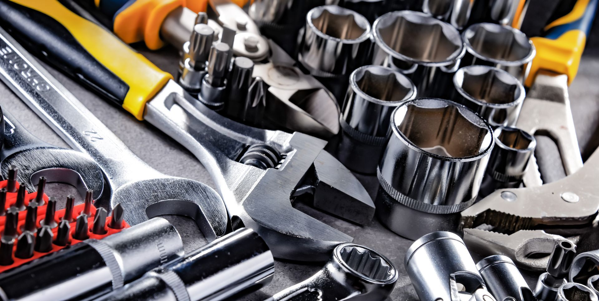 Assorted hand tools, including wrenches, sockets, and pliers, are arranged on a surface.