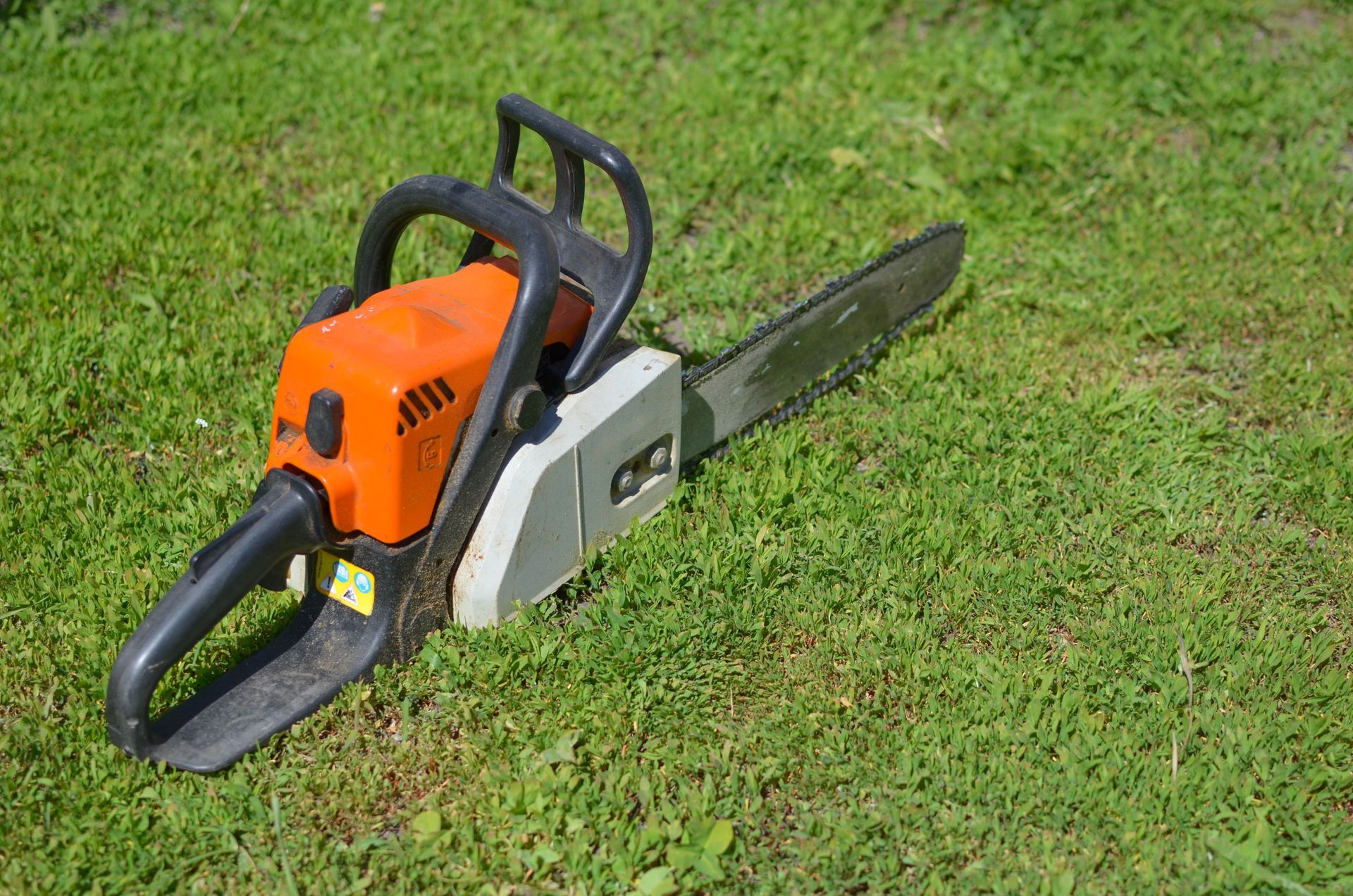 Orange and gray chainsaw resting on green grass.