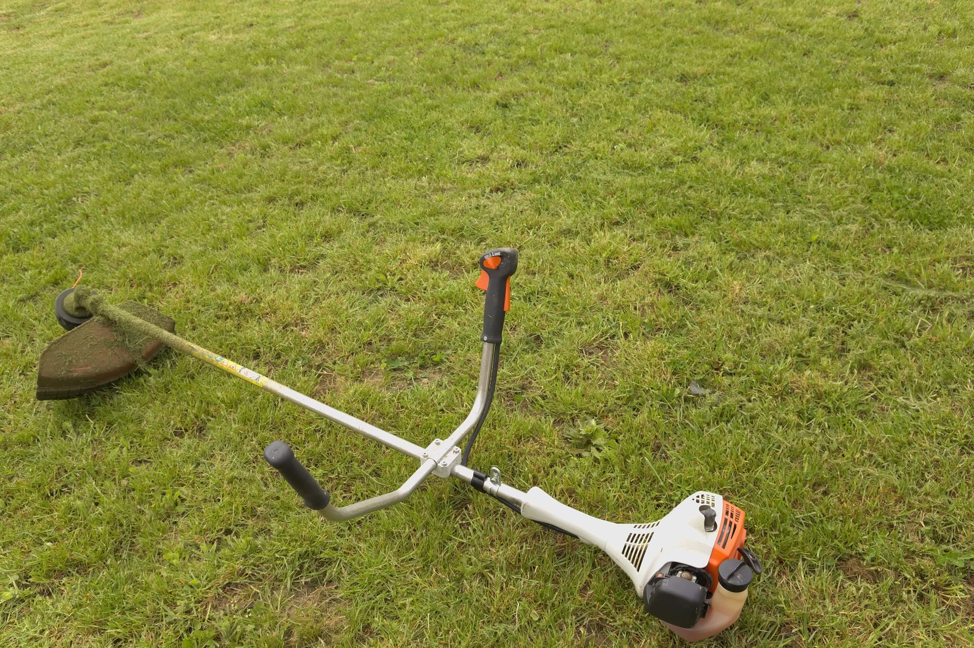 String trimmer lying on green grass.