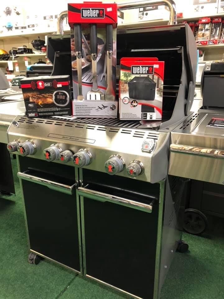 Black metal barbecues on wheels displayed in a store.