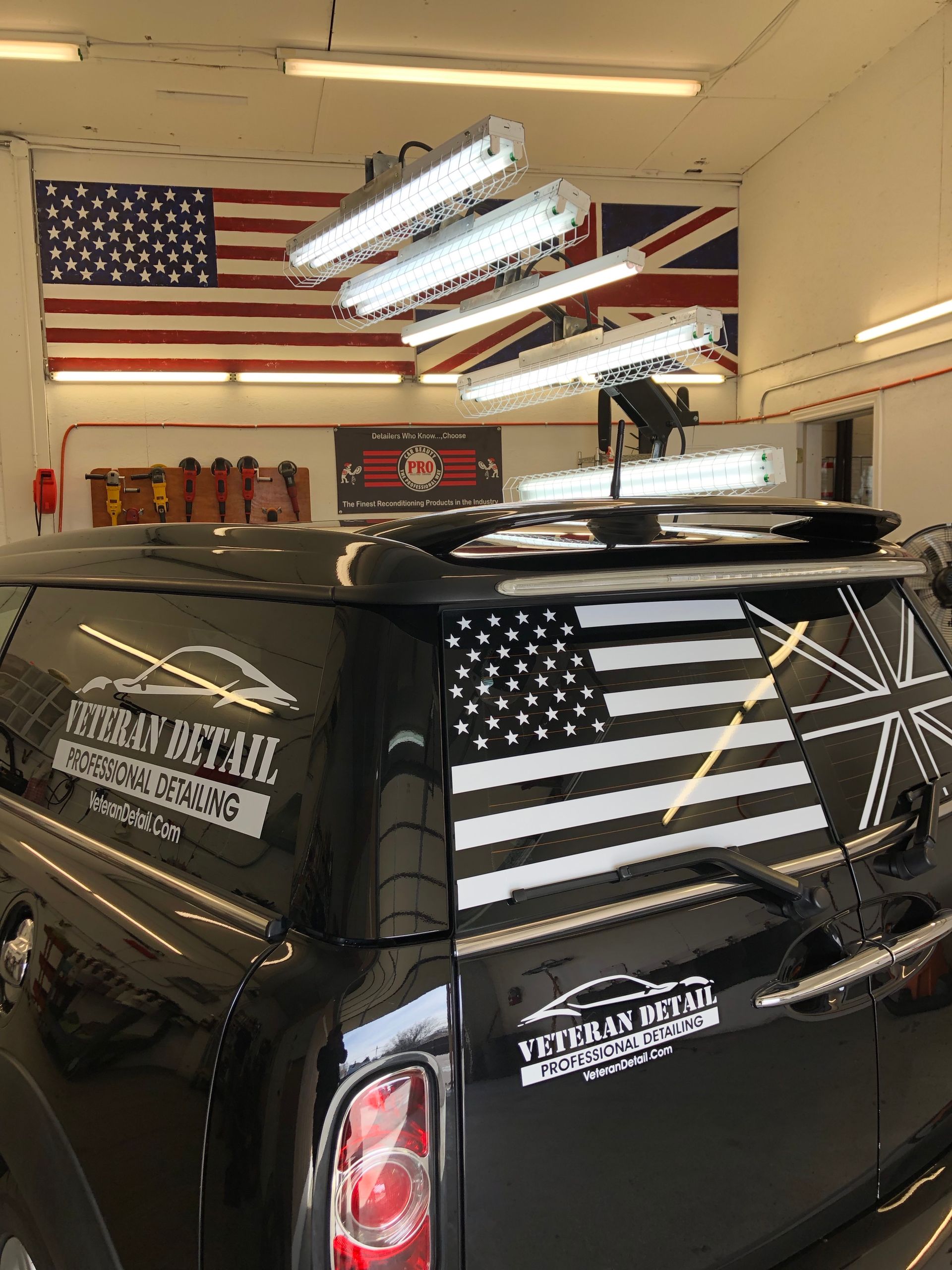 A black car with an american flag on the back window is parked in a garage.