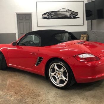 A red sports car with a black top is parked in a garage