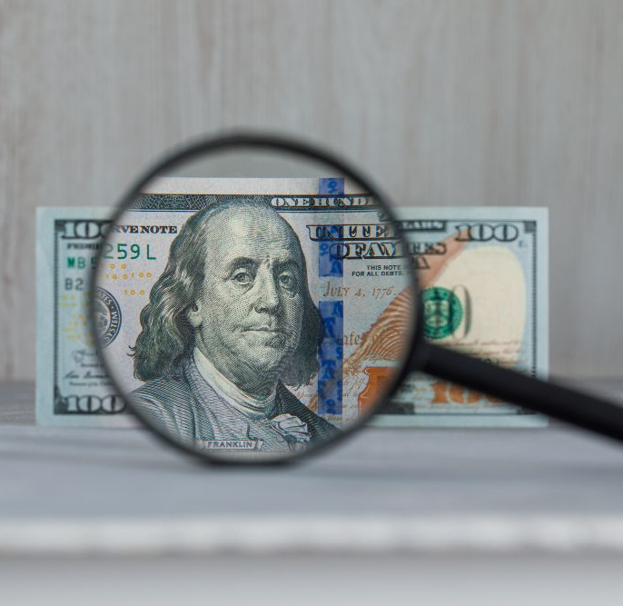 A $100 bill viewed through a magnifying glass, showing a close-up of Benjamin Franklin.