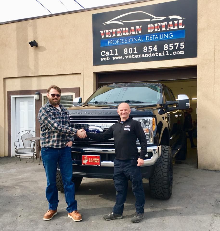 Two men shaking hands in front of a black pickup truck at a car detailing business.