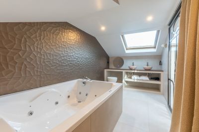 Salle de bain avec baignoire jacuzzi, mur marron texturé, puits de lumière et vanité avec lavabos roses.