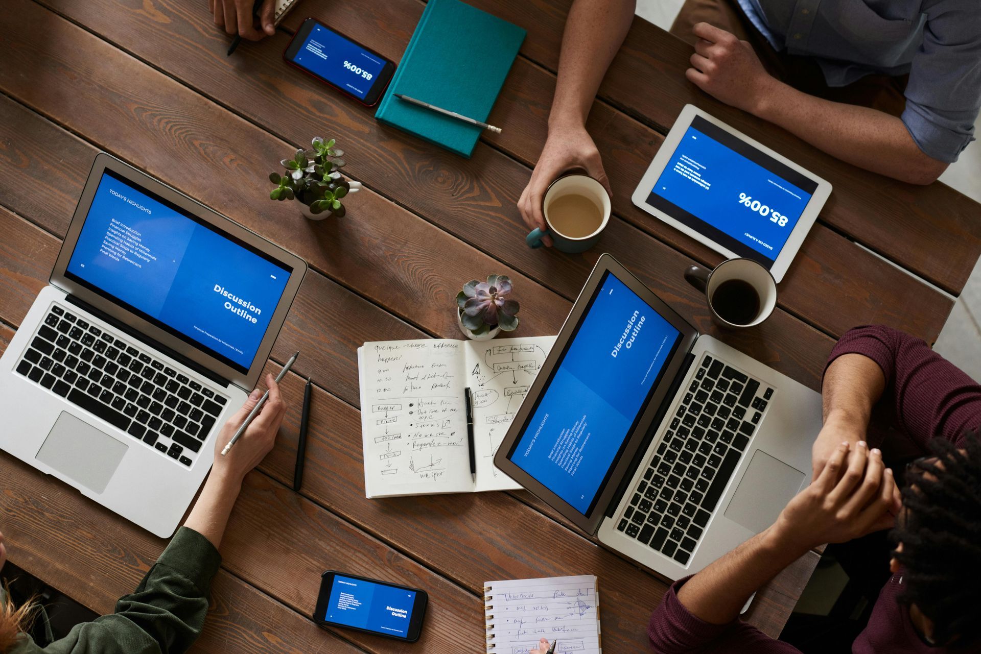 A group of people are sitting at a table with laptops and tablets.