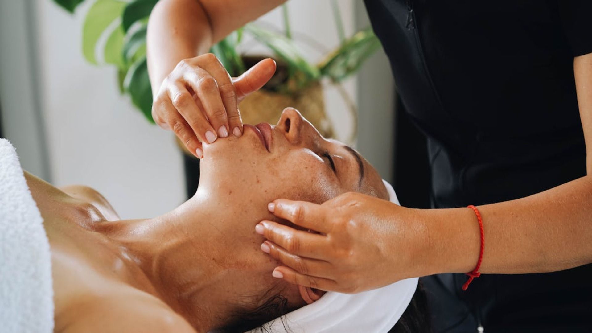 Persona recibiendo un masaje facial en un spa; manos masajeando suavemente el rostro.