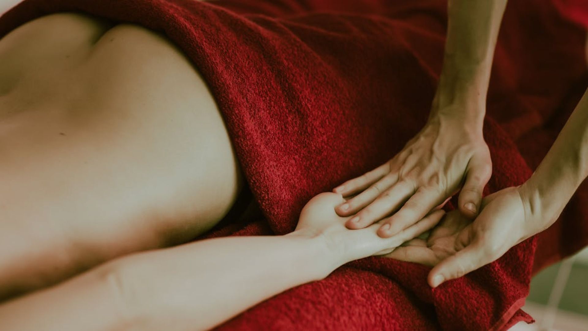 Persona recibiendo masaje en brazo y espalda, envuelta en toalla roja.