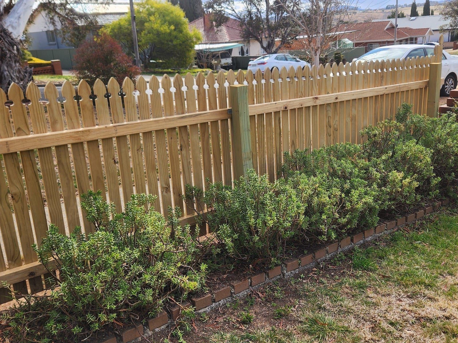 Wooden picket fence with green bushes in front.