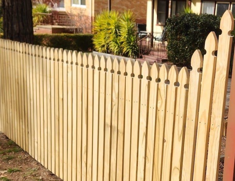 Wooden picket fence in a yard, with pointed tops, brown color.