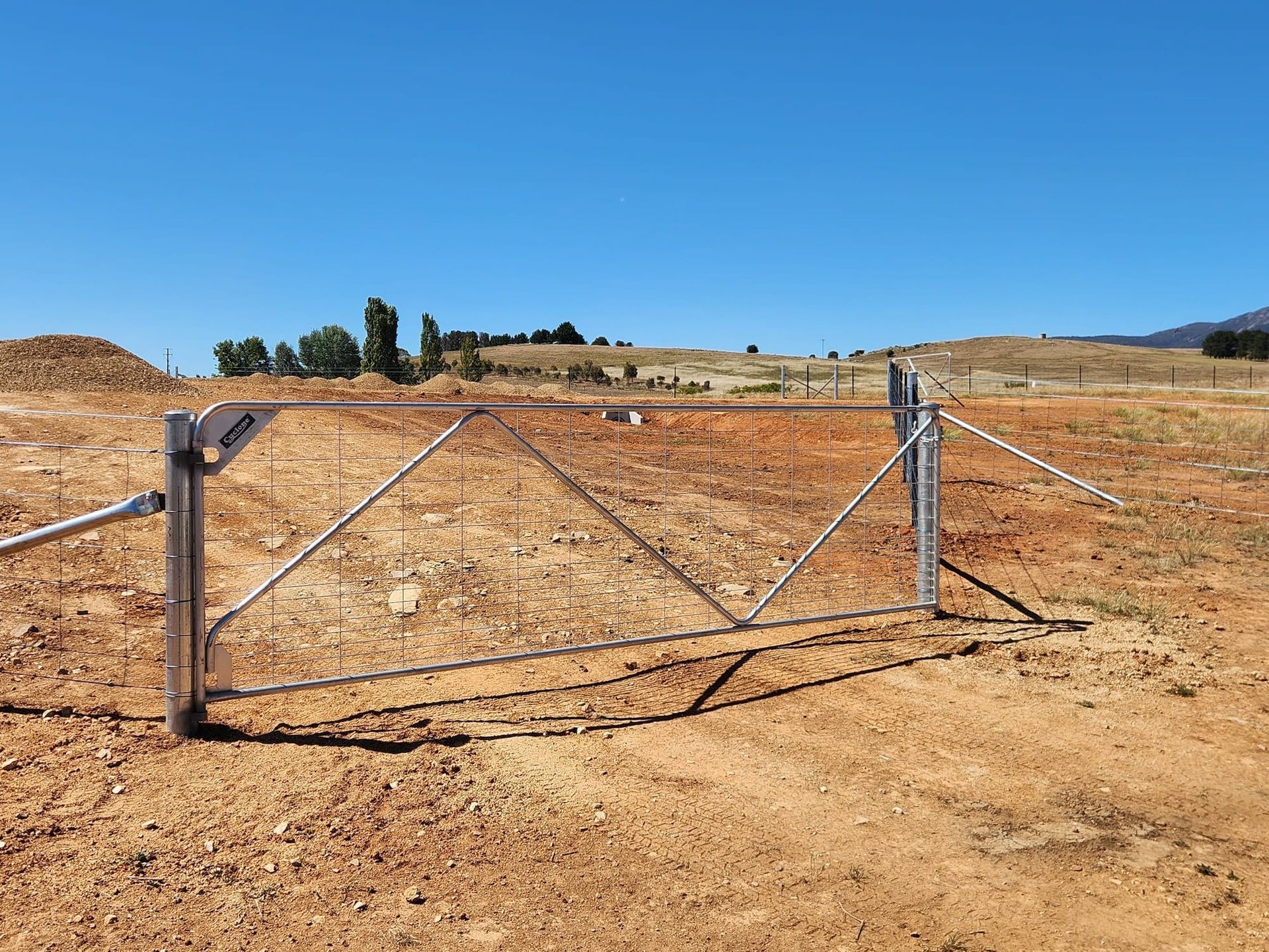Barbed wire fence in a dry field, with a hill in the background under a blue sky.