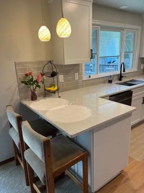 Modern kitchen with white countertops, breakfast bar, pendant lights, and two bar stools.