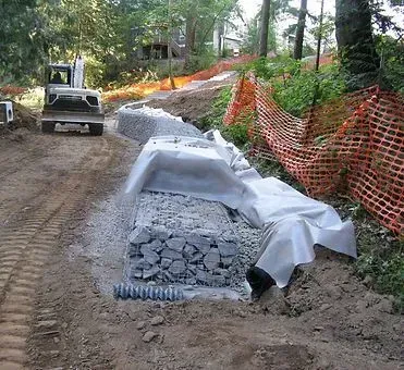 Construction site with an excavator, stone wall, and orange safety fencing.