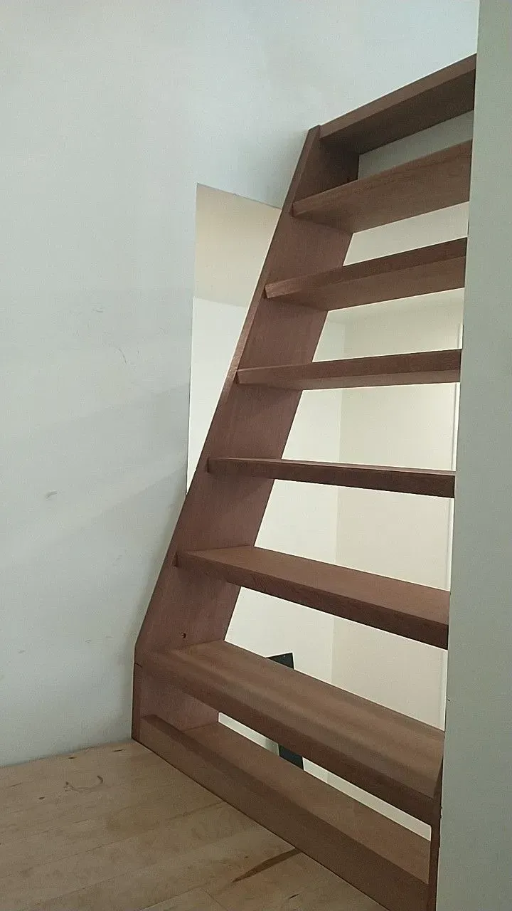 Wooden staircase, brown steps, against white walls.