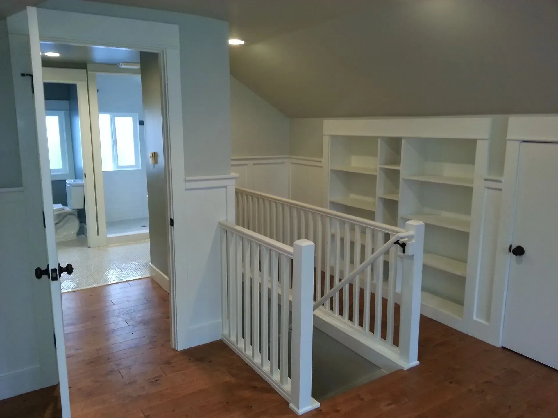 Brightly lit attic bedroom with built-in bookshelves, small staircase, and doorway to a bathroom.