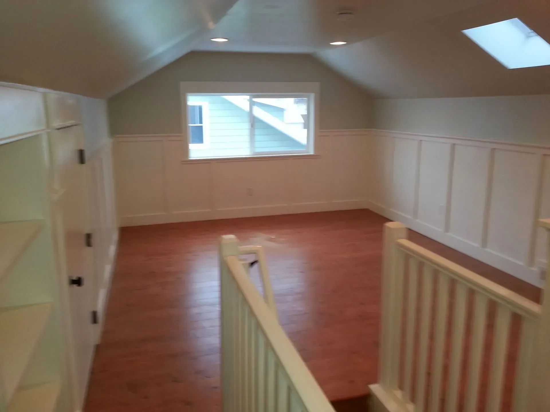 Interior of an attic room with built-in shelves, a window, and a red floor.