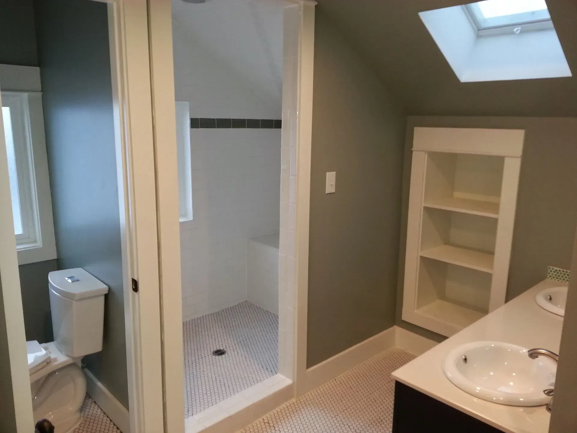 Bathroom with a shower, sink, toilet, and built-in shelving. Green walls, white fixtures, and patterned tile.