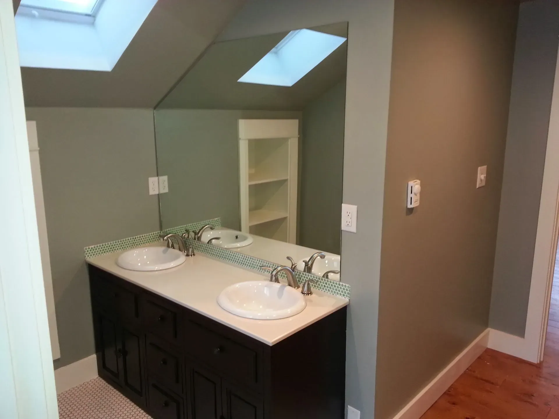 Bathroom with dark brown vanity, two sinks, and large mirror. Gray and brown walls. Skylight.