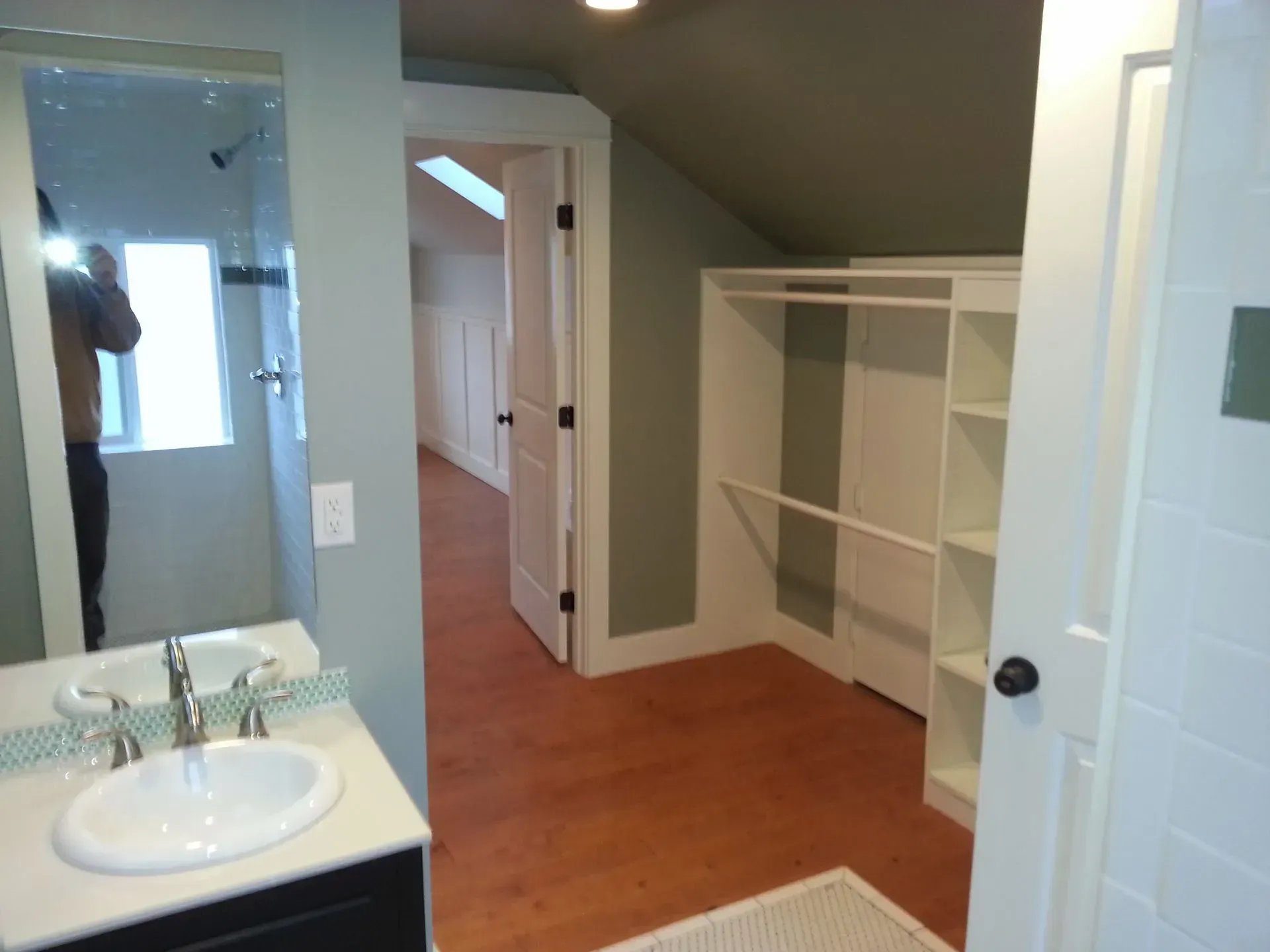 Bathroom with a vanity and mirror, leading to a closet and hallway with a sloped ceiling.