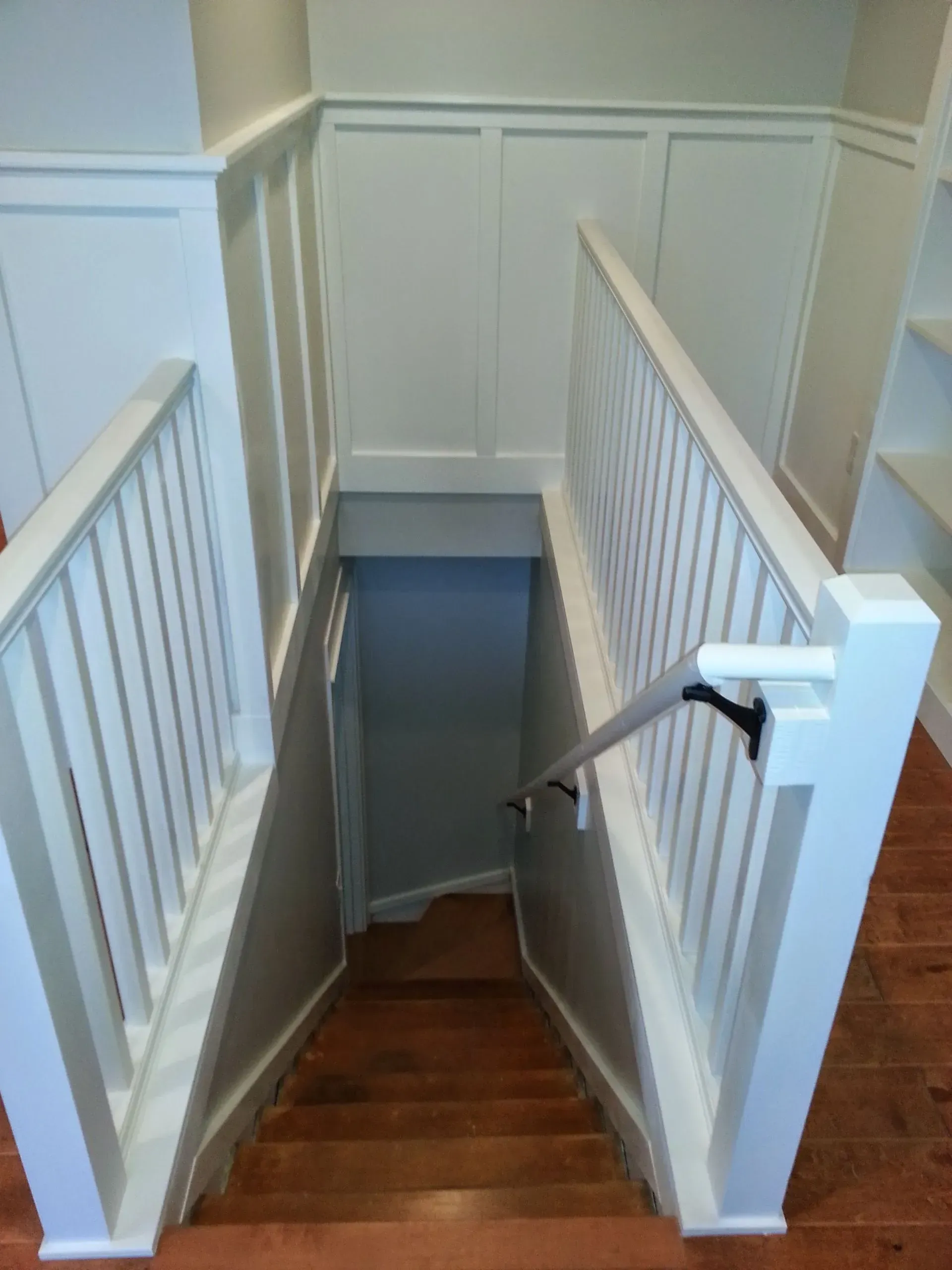 Staircase leading down, with white railings, wainscoting, and wooden steps.