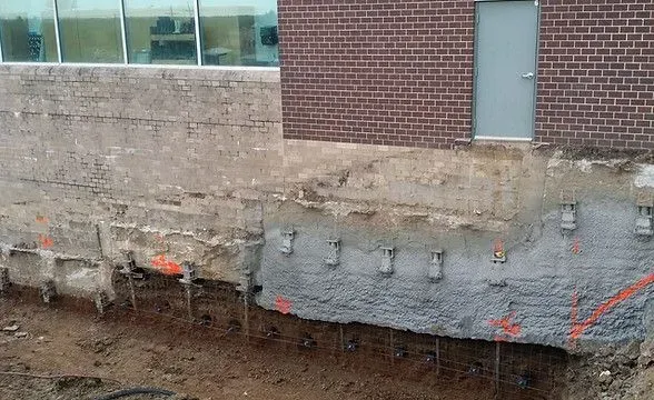 Foundation of a building with exposed concrete and brick, excavation site, metal supports in soil.