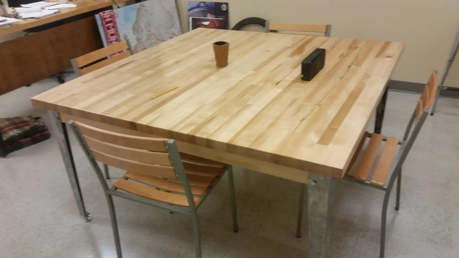 Wooden table with four chairs; a small cup and speaker are on the table.