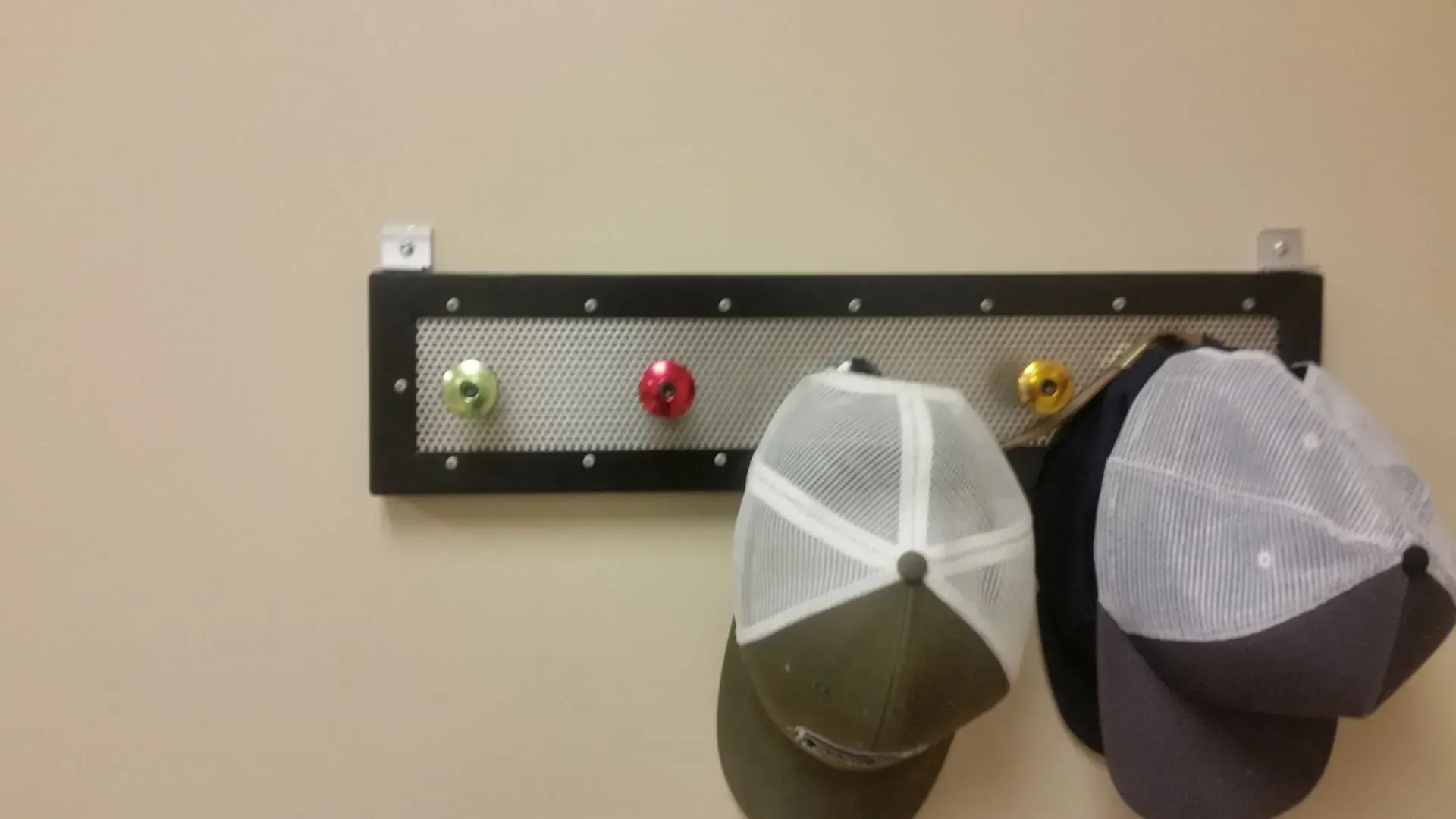 A wall-mounted hat rack with four hats and three ornaments. The rack is black with a mesh front.