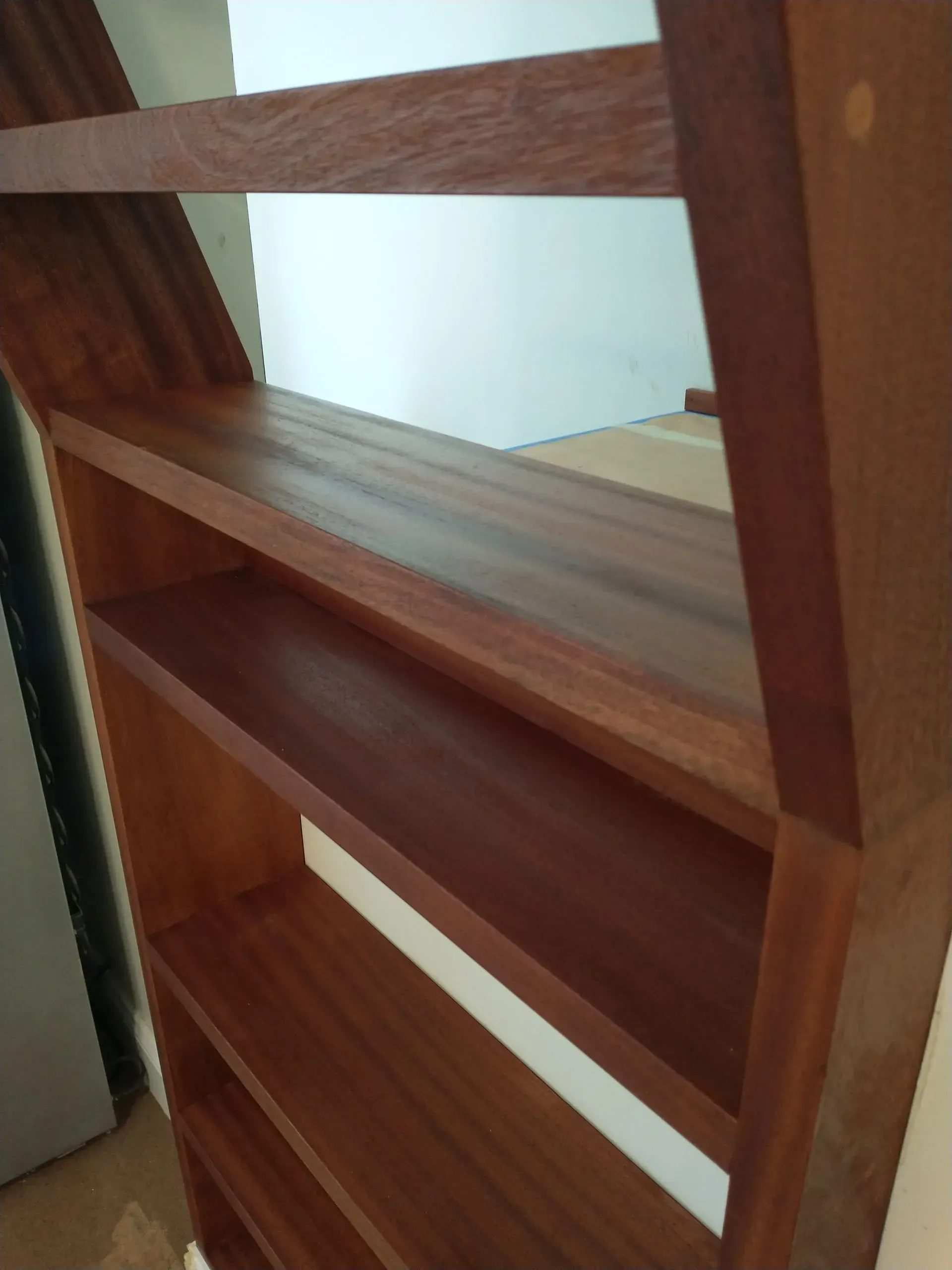 Wooden bookshelf with several shelves, angled and mounted on a wall. Brown wood with a natural finish.
